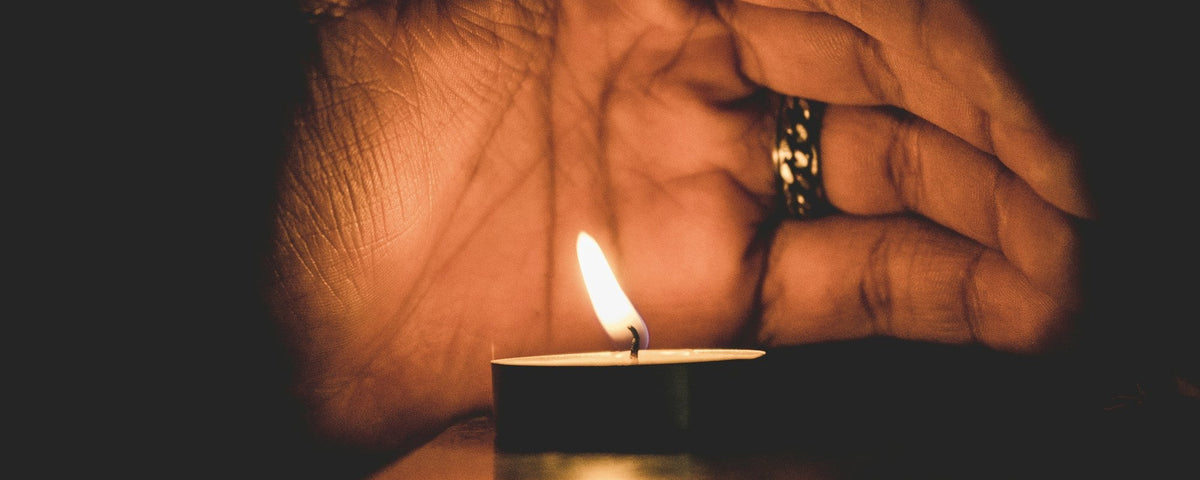 Lighter for older people: an older hand wearing a ring shields a burning tealight